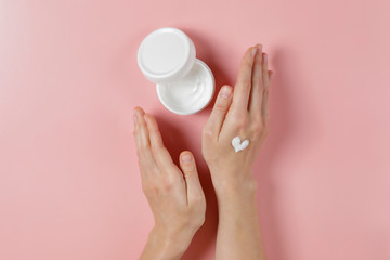 Revitalizing hand cream for healing and recovery after excessive use of soap and disinfectants. Young woman applying moisturizing lotion. Copy space, close up, pink background, flat lay, top view.