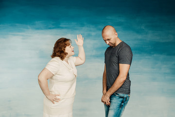 A plump red-haired attractive woman and a tall bald man on a blue background, the wife scolds her...