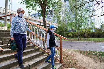 woman and child girl walks down the street during the day, a pedestrian walkway and buildings with apartments, a residential area, a medical mask on their faces protects against viruses and dust