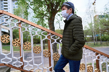 teen boy walks down the street during the day, a pedestrian walkway and high-rise buildings with apartments, a residential area, a medical mask on his face protects against viruses and dust