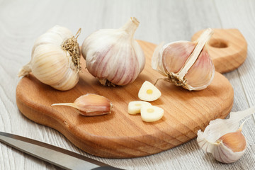 Ripe garlic heads and stainless steel knife on wooden cutting board