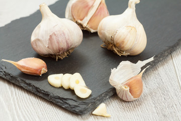 Raw garlic bulbs on a black stone board.