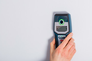 Man hand is scanning wall by cable detector to find a cable before drilling in.