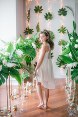 Attractive young girl  in a romantic white dress among tropical greenery and white orchids, roses...