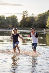 Two happy kids running through water in summer