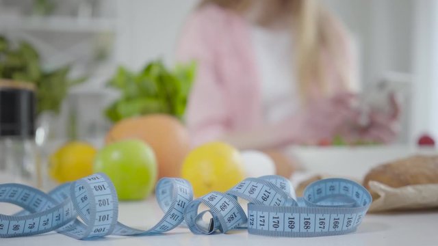 Close-up of measuring tape lying on the table with blurred Caucasian girl counting calories at the background. Healthy Caucasian woman looking after weight. Healthy lifestyle, dieting, beauty.