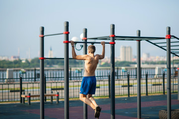 The young man pulls himself up on the horizontal bar on the playground on the promenade.