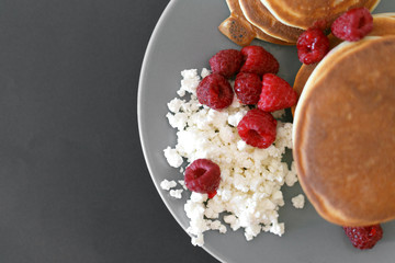 Pancakes with cottage cheese and raspberries on a gray plate, on a black background