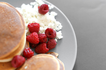 Pancakes with cottage cheese and raspberries on a gray plate, on a black background