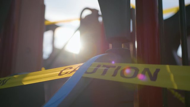 Close up of caution tape on a children's play structure with lens flare from sun in the background