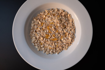 White plate with oat flakes and honey on a dark background