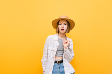 Pretty cheerful girl in light clothing and hat dancing on yellow background. Attractive tourist girl dancing and looking at camera, isolated on orange background.Copy space