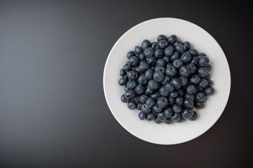 White dish full of blueberries on a black background