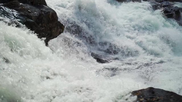 A slow-motion video of the turbulent waters of the Gaula river at the Likholefossen waterfall. A mass of water falling from the rocks, whirling, foaming and splashing around.