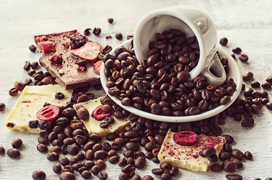 Coffee beans sprinkled from a coffee cup and pieces of chocolate on a rough wooden background. Vintage photo.
