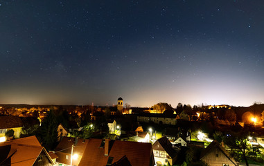 Nächtlicher Blick über Dorf unter Sternenhimmel mit Milchstraße diffus links und...