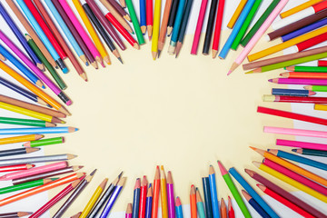 Many colored pencils are arranged around the edges of the image as a frame. In the center is an empty background with space for text. Mock up with copy space.