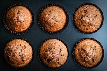Various homemade muffins in a baking dish with berries, chocolate and mint on a dark background top view copy space.