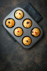 Various homemade muffins in a baking dish with berries, chocolate and mint on a dark background top view copy space.
