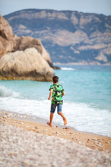 Happy hamdsome teen walks along the sea coast against the background of the sea, from behind a beautiful landscape