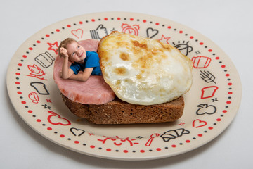 creative work: a boy lies on a toast bread with an egg and sausage on a plate on a light background