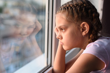 Tired of self-isolation, a bored quarantine girl looks out the window