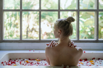 Young adult girl lying in bathtub with herbs and flowers