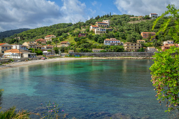 Fototapeta premium Beautiful summer landscape of the resort with turquoise sea water, village with colorful houses and mountains on the horizon and blue sky. Corfu Island, Greece.
