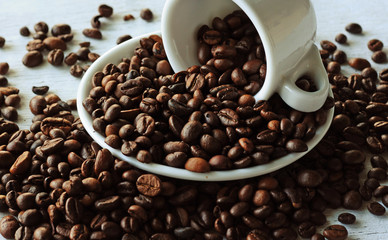 Coffee beans scattered from a coffee cup on a rough wooden background. Vintage photo.
