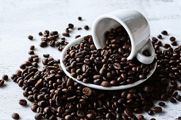 Coffee beans scattered from a coffee cup on a rough wooden background. Vintage photo.