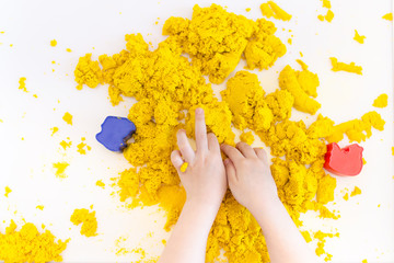 Yellow magic sand in a kids hands on a white background close up. Early sensory education. Preparing for School. Development - obrazy, fototapety, plakaty