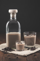 Bottle and glasses of Cream coffee liqueur with ice, and coffee  beans on rustic wooden background.