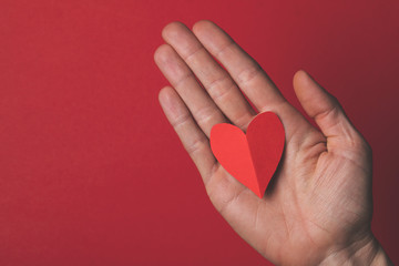 Female hand holding a red paper cut out heart on a plain red background.