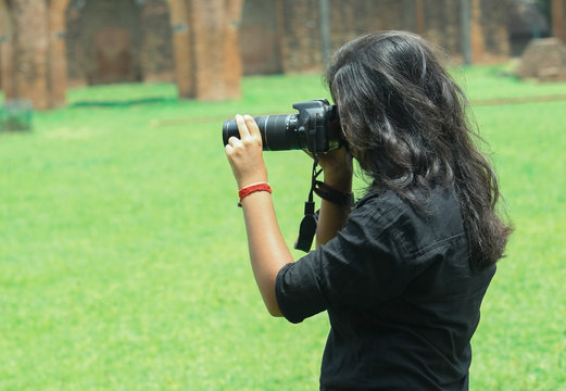 A young girl woman taking photos by DSLR camera keeping her eye in the viewfinder of the camera wearing black shirt.outdoor park tourist place