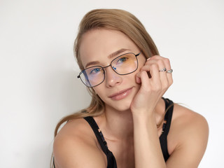 Headshot portrait of a cute natural looking blonde woman wearing simple black blouse and nerd glasses posing on a white background resting chin on hand