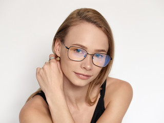 Headshot portrait of a cute natural looking blonde woman wearing simple black blouse and nerd glasses posing on a white background touching her ear