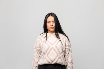 Portrait of a young beautiful cute brunette girl in a warm winter sweater on light gray background.