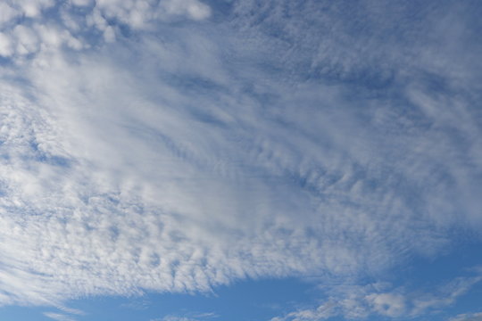 White altocumulus clouds and bright blue sky background.