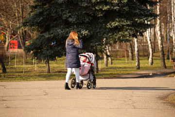 Young mother with a child in a pram talking on a mobile phone. Walk a girl with a son or daughter....