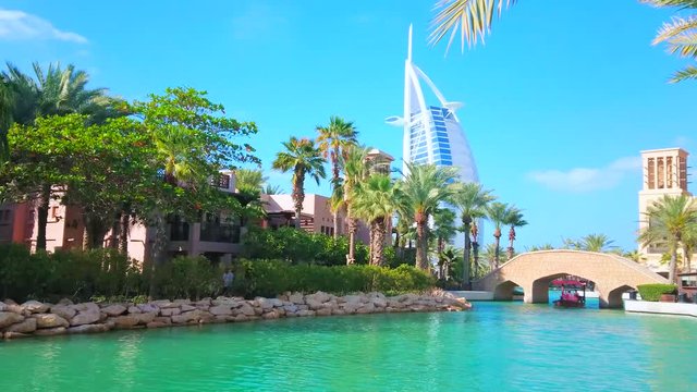 The canal of Souk Madinat Jumeirah with boats, footbridge and a view of Burj Al Arab, Dubai, UAE
