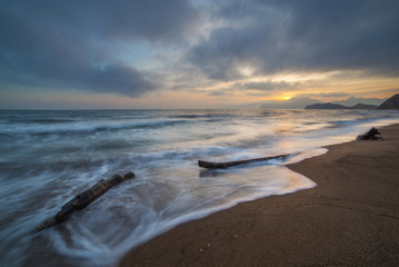 Long exposure seascape with beach and mountains at sunset