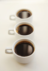 Black coffee in white cups one after another on white background