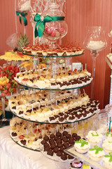 Candy bar. White wedding cake decorated by flowers standing of festive table with deserts, strawberry tartlet and cupcakes. Wedding. Reception Tartlets