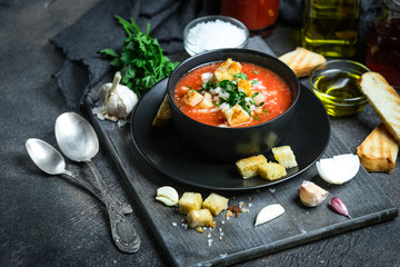 Traditional spanish cold tomato soup gazpacho in a bowl over black slate, stone or concrete background.Top view with copy space.