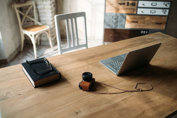 Workplace - wooden table with books, computer, glasses and camera