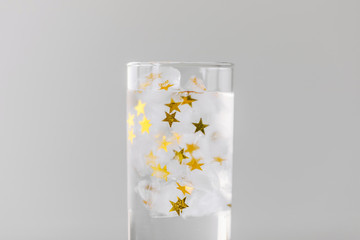 Ice cubes with frozen golden stars in a glass of water. Concept of universe and astrology.