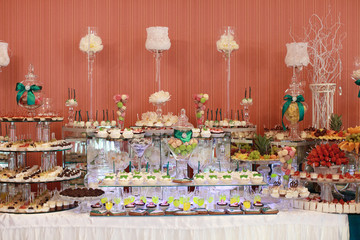 Candy bar. White wedding cake decorated by flowers standing of festive table with deserts, strawberry tartlet and cupcakes. Wedding. Reception Tartlets