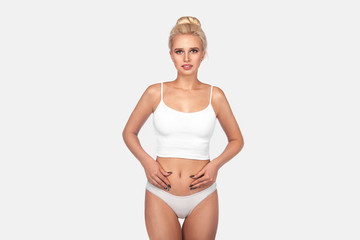 Fototapeta premium Young, healthy and beautiful blonde woman in white lingerie. Sport, fitness, diet, weight loss and healthcare concept. Slim female belly, girl holding her skin for cellulite check.