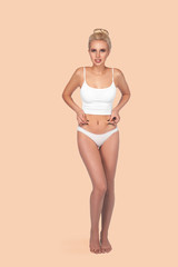 Young, healthy and beautiful blonde woman in white lingerie. Sport, fitness, diet, weight loss and healthcare concept. Slim female belly, girl holding her skin for cellulite check.