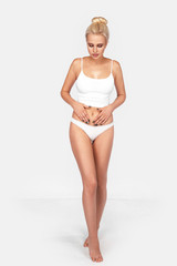 Young, slim, healthy and beautiful blonde woman in white lingerie holds his hands on his stomach. Sport, fitness, diet, weight loss and healthcare concept. Mockup.